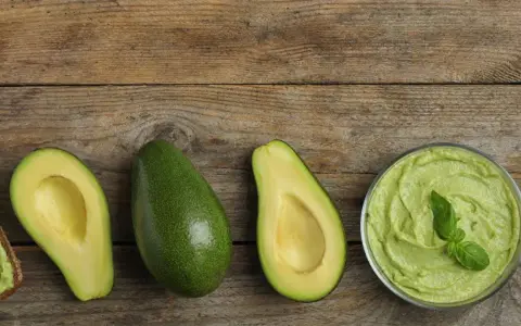 Avocado lagern: Ganze und halbe Avocados, Guacamole in einer Schüssel und Avocado-Toast auf Holzuntergrund.