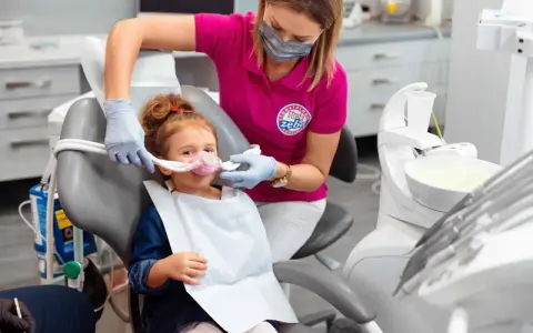Dziecko w masce do sedacji wziewnej. Dentystka monitoruje stan pacjenta, minimalizując potencjalne skutki uboczne.