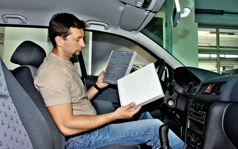 Mężczyzna w kabinie Renault Megane 3 porównuje stary i nowy filtr kabinowy, przygotowując się do jego wymiany.