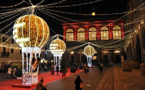 Luci scintillanti e palloni luminosi creano un'atmosfera magica per un week end a Rimini. Persone passeggiano su un tappeto rosso, ammirando le decorazioni natalizie.