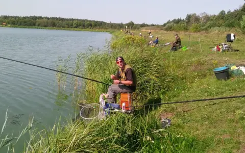 Wędkarz siedzi nad jeziorem, przygotowując się do łowienia. Czy to bat, czy inna wędka, ważne, że relaks nad wodą.