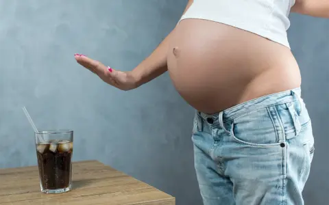 Schwanger und verzichtet auf Cola. Eine Hand weist ein Glas Cola mit Eis und Strohhalm ab.