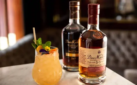 Ein erfrischender Cocktail mit Minze und Früchten neben zwei Flaschen Dos Maderas Rum. Der Alkoholgehalt des Rums ist auf dem Etikett angegeben.