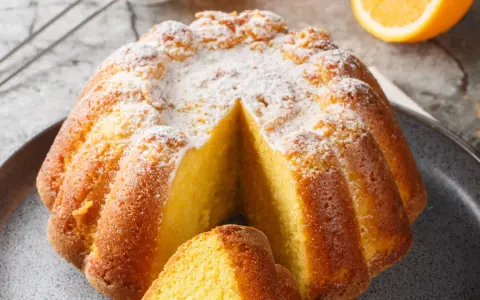 Una fetta di torta all'arancia morbidissima, cosparsa di zucchero a velo, pronta per essere gustata.