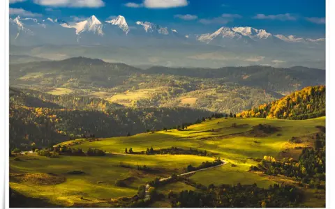 Widok na Tatry z ośnieżonymi szczytami, w tym Trzy Korony. Jesienne wzgórza pokryte złotymi liśćmi i zielonymi łąkami.