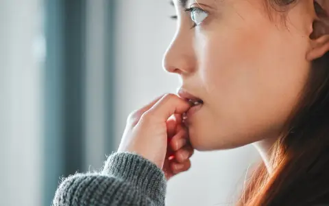 Une jeune femme se ronge les ongles, un signe de stress ou d'anxiété. La signification psychologique de se ronger les ongles est souvent liée à une recherche de réconfort.