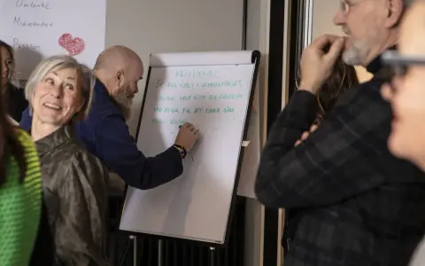 En grupp människor diskuterar hur en bra chef ska vara. En man skriver på en whiteboard om medvetenhet och utveckling.
