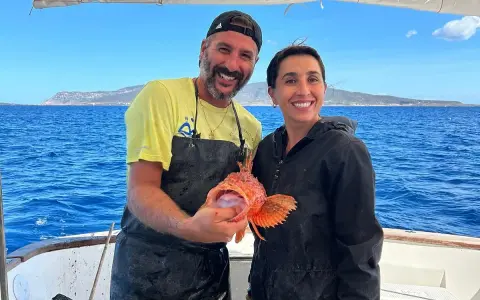 Coppia felice in barca, lui mostra un pesce rosso appena pescato, un'esperienza di pesca turismo indimenticabile.