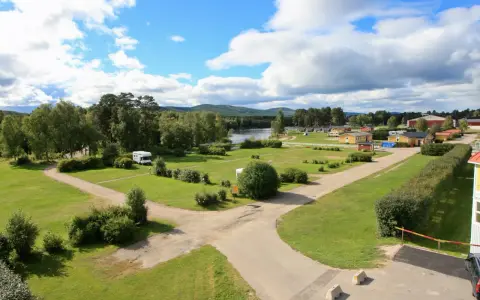Vacker vy över svegs camping med husbilar, stugor och en sjö i bakgrunden under en molnig himmel.