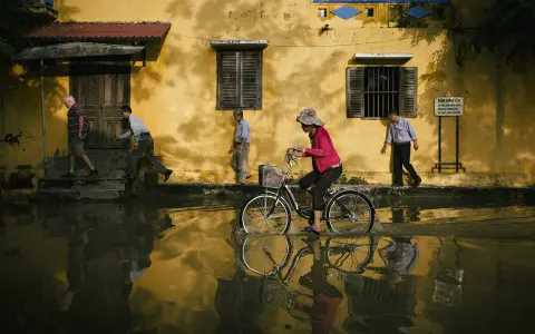 Une femme à vélo traverse une rue inondée, reflétant la vie quotidienne. Quel objectif pour photo de rue capture cette scène ?