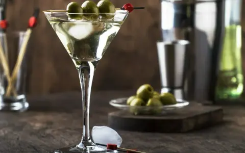 Elegancki martini z oliwką, gotowy do degustacji. Obok kostki lodu i talerzyk z oliwkami.