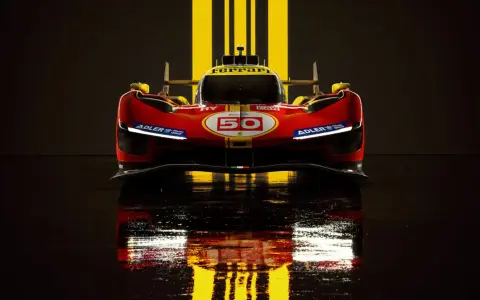 Wyścigowy Ferrari 499P w czerwono-żółtych barwach, z numerem 50, odbija się w mokrej nawierzchni.