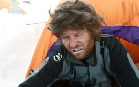 Zmęczony alpinista z białym proszkiem na ustach, być może lek na chorobę wysokościową, w namiocie na śniegu.