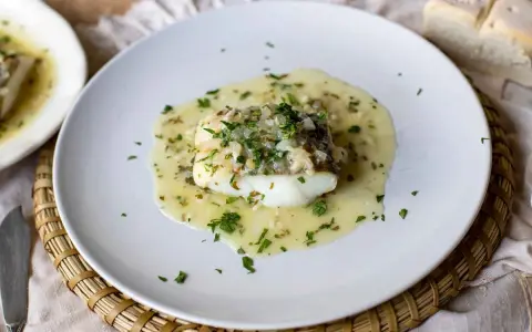 Un delicioso bacalao en salsa verde, con perejil fresco picado y trozos de pan al lado.