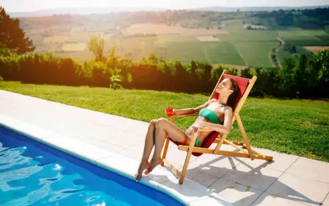 Donna rilassata su una sdraio, con drink, vicino a una piscina. Il sole splende, ideale per chi vuole sapere come abbronzarsi velocemente.