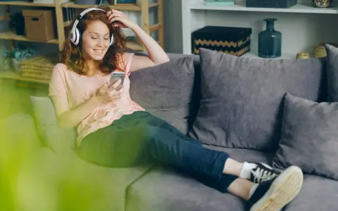 Dziewczyna z rudymi włosami słucha muzyki Indili, przeglądając telefon na kanapie. Jej uśmiech sugeruje, że to jej ulubiona love story.