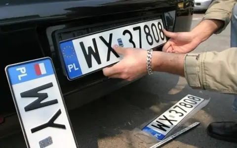 Montaż nowych tablic rejestracyjnych. Jedna z nich, z numerem WX 37808, jest właśnie wkładana. Obok leży kolejna, jeszcze w folii.