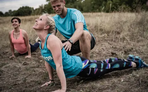 Ein Trainer unterstützt eine Frau bei einer Yoga-Übung im Freien. Das **Faszien Training** stärkt die Körpermitte.