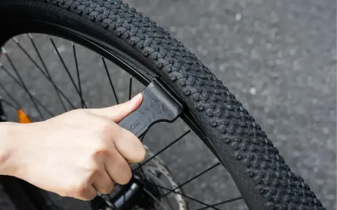 Dłoń używa czarnej łyżki do opon rowerowych, aby zdjąć oponę z obręczy. To proste narzędzie, które ułatwia wymianę dętki.