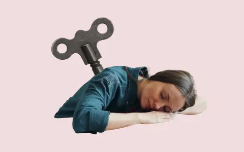 En kvinna sover med en uppdragnyckel i ryggen, som om hon är en trasig leksak. Man kan spy av stress när man är helt slutkörd.