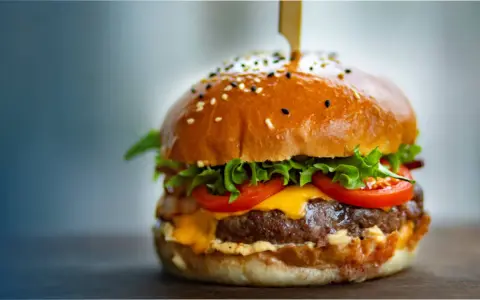 Un délicieux burger, avec sa brioche dorée, sa viande juteuse, son fromage fondant, sa laitue croquante et ses tomates fraîches. On se demande d'où vient le burger, ce classique indémodable.