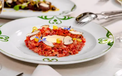 Delicioso tartar de atún fresco, adornado con láminas de trufa negra, flores comestibles y un toque de amarillo vibrante.