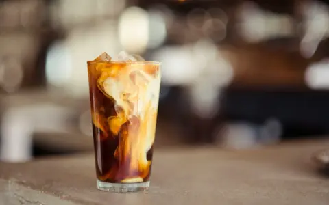 Ein Glas mit Eiswürfeln und einem cremigen Strudel aus Milch und Kaffee. Ein erfrischender Cold Brew Latte.