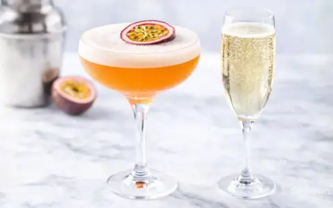 Pomarańczowy drink z pianką i marakują, obok kieliszek szampana. Idealny white lady drink na letnie popołudnie.