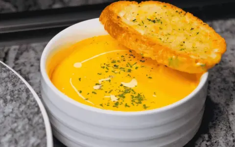 Bol de soupe orange crémeuse garni d'herbes et d'une tranche de pain à l'ail.