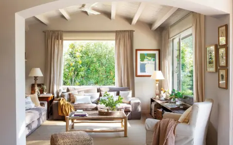 Salón acogedor con sofás en color greis, mesa de centro de madera y gran ventanal con vistas a la vegetación.