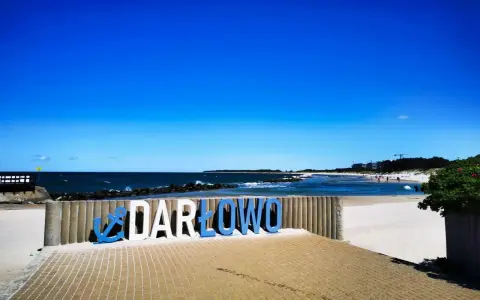 Napis "DARŁOWO" na tle plaży i morza. Darłówko zaprasza na wypoczynek nad Bałtykiem.
