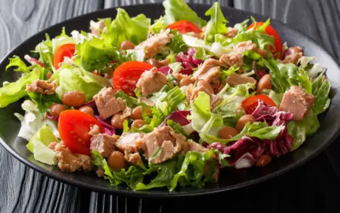 Ein frischer Thunfischsalat mit knackigem Salat, Tomaten und Bohnen auf einem schwarzen Teller.