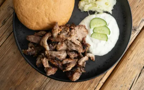 Ein Teller mit gegrilltem Fleisch, einem Brötchen, Tzatziki und Krautsalat. Perfekt für ein leckeres Gyros Rezept.