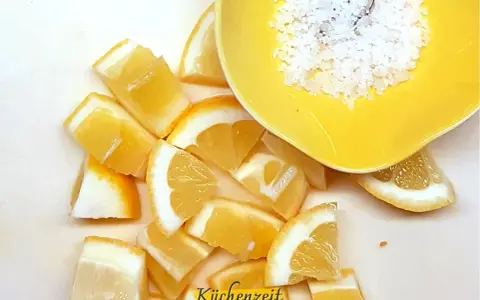 Frische Zitronenspalten und grobes Salz in einer gelben Schale – die perfekte Basis für viele Rezepte mit Zitrone.