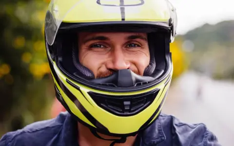 Uśmiechnięty mężczyzna w żółtym kasku motocyklowym z czarnymi elementami.