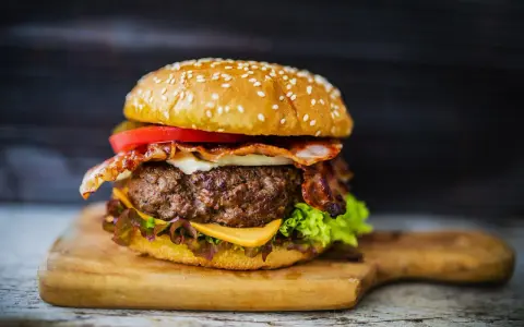 Soczysty burger z bekonem, serem i warzywami na desce.