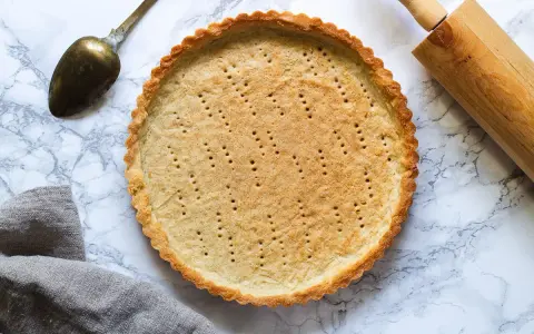 En gyllene pajskal, perfekt för ditt pajdeg recept. En kavel och en gammal sked ligger bredvid.