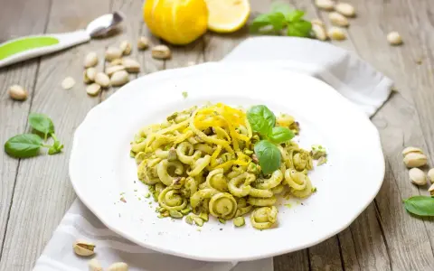 Makaron orecchiette z zielonym pesto, pistacjami i skórką cytrynową na białym talerzu.
