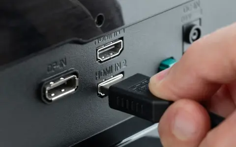 Hand steckt HDMI-Kabel ein, um den PC mit dem Fernseher zu verbinden. Anschlüsse für DisplayPort und HDMI sind sichtbar.