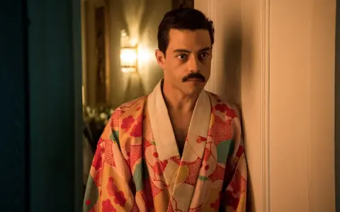 Freddie Mercury w barwnym szlafroku, jakby zrodzony z **bohemian rhapsody**, opiera się o drzwi.