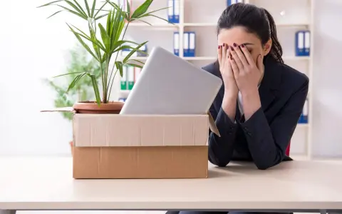 Verzweifelte Frau mit Karton und Laptop im Büro. Sie muss eine innerbetriebliche Versetzung ablehnen und ist sichtlich mitgenommen.