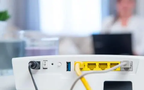 Router vom Strom trennen wie lange? Das Bild zeigt die Rückseite eines weißen Routers mit Netzteilanschluss, Schalter und LAN-Ports.