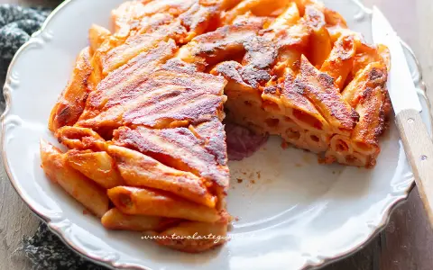Una deliziosa frittata di pasta, dorata e croccante, servita su un piatto bianco con un coltello.