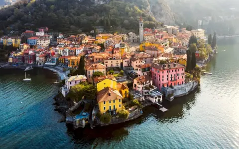 Färgstark by vid en sjö i norra Italien, med hus i gult, rosa och orange som klättrar uppför en sluttning.