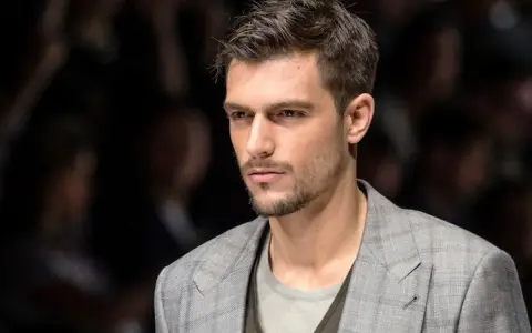 Uomo con capelli spettinati, sguardo intenso, indossa una giacca a quadri grigia.