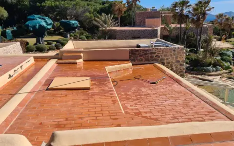 Proceso de impermeabilizar terraza con acabado de tejas rojas. El sol brilla sobre la superficie mojada, lista para proteger la casa.