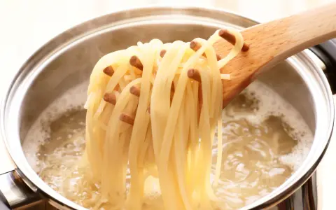 Une louche en bois retire des spaghettis bouillis à la perfection, juste al dente, d'une casserole d'eau bouillante.