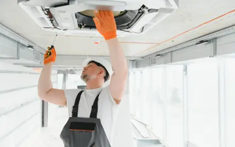 Técnico revisa aire acondicionado en techo, una señal para saber si le falta gas al aire acondicionado es que no enfría.