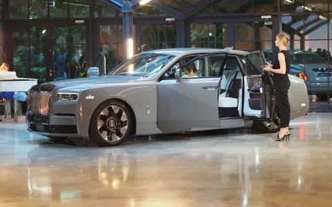 Elegancki szary Rolls-Royce Phantom z otwartymi drzwiami, obok którego stoi kobieta. Poznaj jego wyjątkową rolls royce phantom cena.