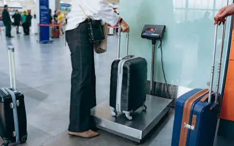 Osoba ważąca bagaż rejestrowany na wadze w terminalu lotniczym.